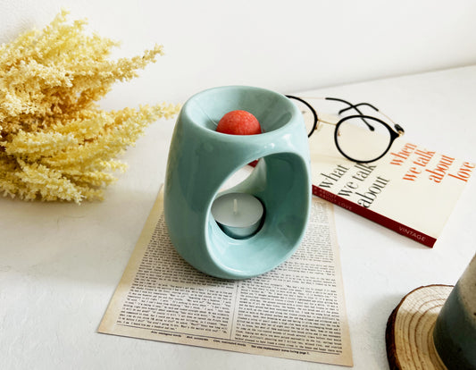 Orange wax melt sits in a green candle wax burner beside flowers, book and glasses