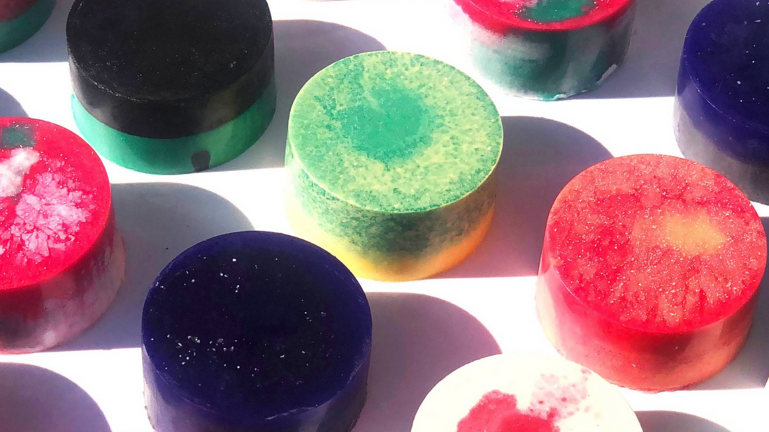 Circular vegan soap bars in a range of colours lie on a white table