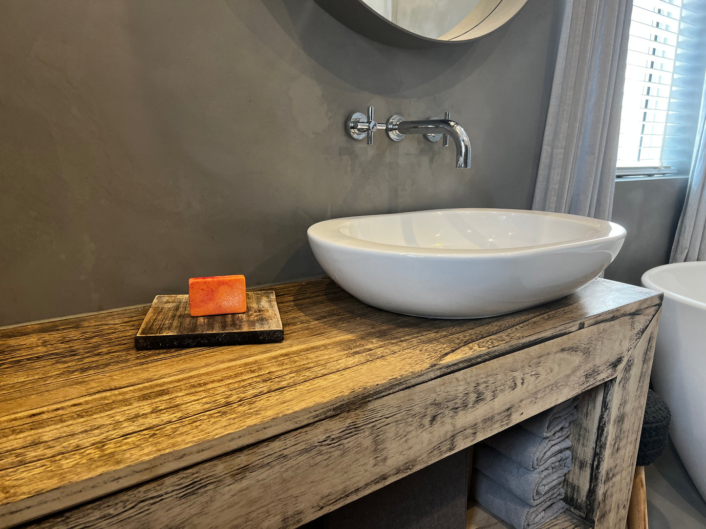 A red and orange rectangle bar soap, placed on a wooden sink counter. A white sink and silver taps are next to the soap