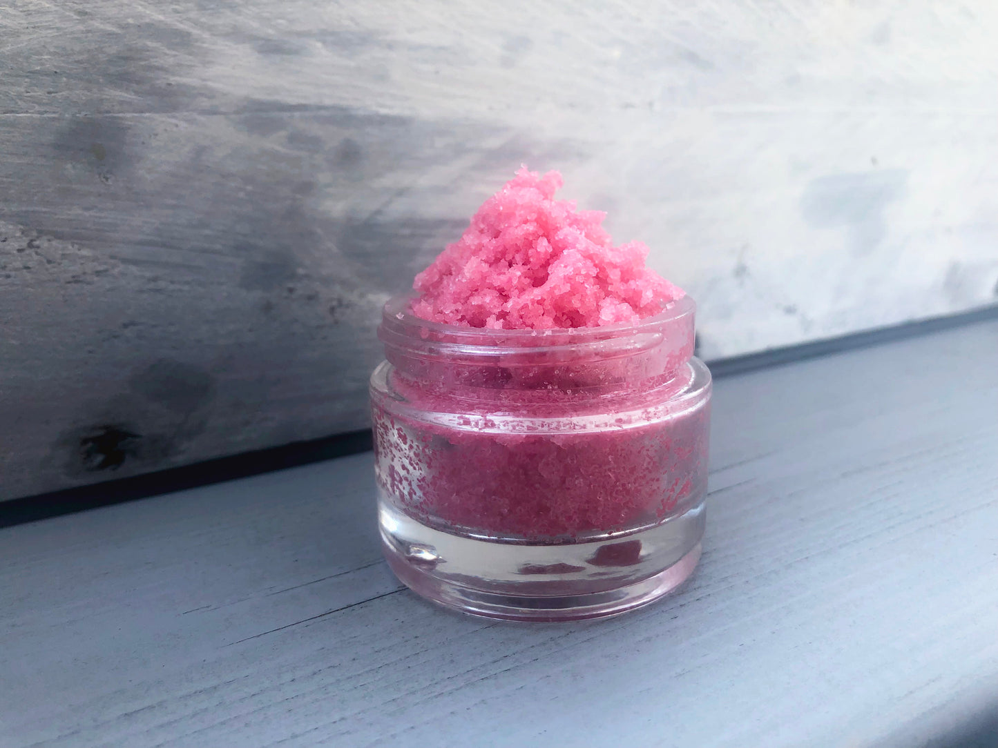Pink strawberry sugar lip scrub used for exfoliating in a glass jar